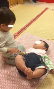 仰向けになっている当時約6ヶ月の子の顔を覗き込む当時約1歳4ヶ月の女の子です。